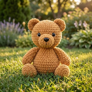 May include: A handmade, crochet teddy bear in a warm, golden-brown color. The bear has a round head, small ears, and a black nose. It is sitting on green grass, with its arms and legs extended. The bear is a soft, cuddly toy.