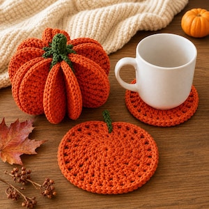 May include: A crocheted orange pumpkin with a green stem, a matching round orange crocheted coaster under a white ceramic mug, and a small orange pumpkin, all featuring textured yarn stitches in a vibrant autumn-inspired orange color.