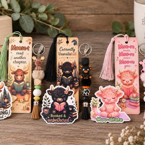 May include: Three rectangular bookmarks with tassels, three matching beaded keychains with animal charms, and three die-cut stickers featuring illustrated cows and moose. The items display text including Moose-t read another chapter, Currently Unavailabull, Moo-re books, Just Moosing Around, Booked & unbothered, and Moo-ditate.