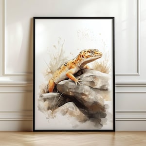 May include: A framed watercolour print of a leopard gecko on a rock. The gecko displays orange, yellow, and brown markings. The artwork is set against a soft, neutral background with subtle plant details.