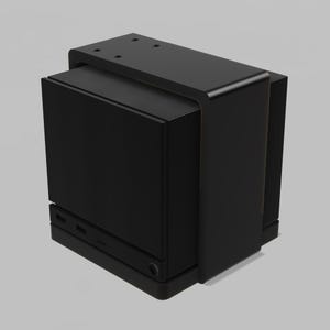 Könnte beinhalten: Ein mattschwarzes, würfelförmiges elektronisches Gerät mit einer glatten, soliden Frontplatte und einem U-förmigen Rahmen, der über die Oberseite verläuft. Die Basis enthält zwei rechteckige Anschlüsse und einen kleinen runden Knopf an der Unterkante.