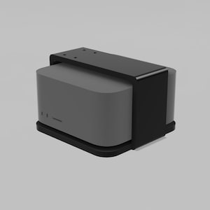 Puede incluir: Un dispositivo rectangular gris con una parte superior e inferior negras. El dispositivo tiene un diseño curvo y un soporte negro en la parte superior. El dispositivo está sobre un fondo gris claro.