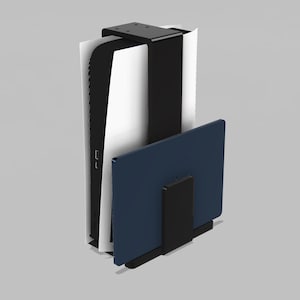 Puede incluir: Un soporte de pared de metal negro que sostiene una consola de juegos blanca y negra en posición vertical, con un dispositivo electrónico rectangular azul oscuro asegurado en un soporte secundario de metal negro fijado al frente.