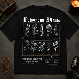 May include: Black t-shirt featuring a detailed botanical illustration of poisonous plants. The design includes the text "Poisonous Plants" and "Beautiful Plants" in an ornate font, along with a list of plant names and the phrase "Some poisons cloud the eyes. Others clear them."