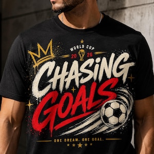Könnte beinhalten: Schwarzes T-Shirt mit einem Fußball-Motiv. Das Design enthält die Worte "CHASING GOALS" in Weiß und Rot, einen Fußball, eine goldene Krone und den Text "WORLD CUP 2026". Der Satz "ONE DREAM. ONE GOAL." ist ebenfalls enthalten.