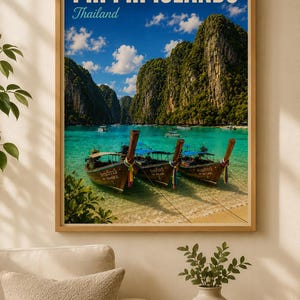May include: A framed print of Phi Phi Islands, Thailand. The image shows a turquoise bay with longtail boats, lush green cliffs, and a blue sky with clouds. The print is in a wooden frame.