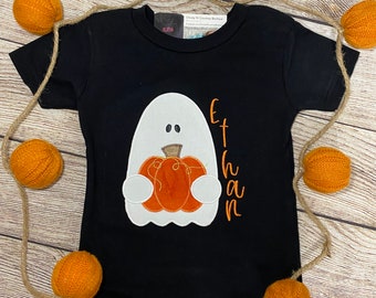 May include: Black t-shirt with a white ghost holding an orange pumpkin. The text "Ethan" is embroidered on the shirt.