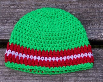 May include: A handmade crochet beanie in bright green, with a red and white striped band. The hat is made of soft yarn and is suitable for all seasons. The hat is a festive accessory.