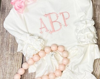 May include: White long-sleeve shirt with pink ruffled sleeves and a pink embroidered monogram "ABP".