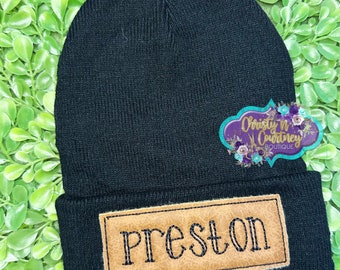 May include: Black knit beanie with a brown leather patch that says "Preston" in a stitched font.