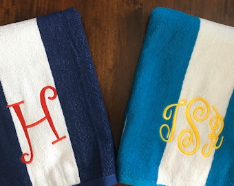 May include: Two striped beach towels. One is navy blue with a white stripe and a red embroidered letter "H". The other is light blue with a white stripe and a yellow embroidered monogram "TSR".