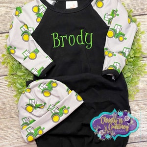 May include: A black and white baby sleeper with green tractor print on the sleeves. The sleeper has a black and white hat with green tractor print. The sleeper has the name "Brody" embroidered on the front.