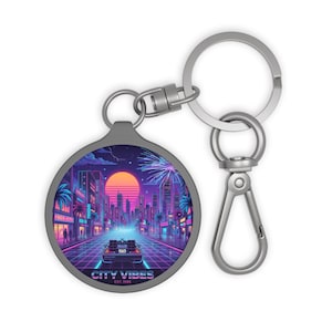 May include: A silver-toned keychain with a round pendant featuring a retro cityscape design. The artwork showcases a vibrant sunset, palm trees, and a futuristic car, with the text "CITY VIBES EST. 1985" at the bottom. The keychain has a clasp and a ring.