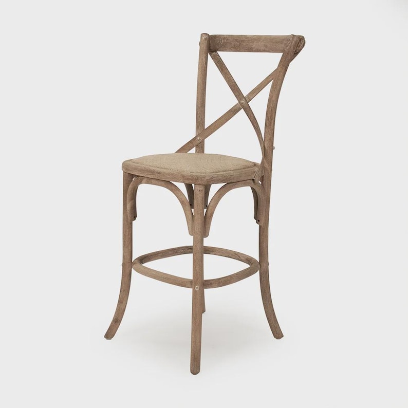 Puede incluir: Taburete de bar de madera con acabado natural. El taburete presenta un respaldo en forma de X y un reposapi&eacute;s redondo. El asiento est&aacute; tapizado en tela de color neutro. El dise&ntilde;o es r&uacute;stico y adecuado para una cocina o bar.