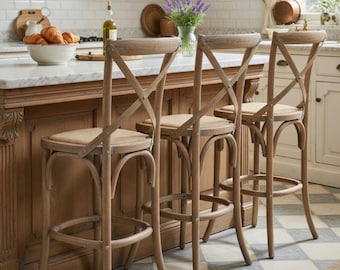 May include: Three wooden bar stools with woven seats and an X-shaped backrest. The stools have a curved design and a footrest. The stools are in a kitchen setting with a marble countertop and a wooden island.