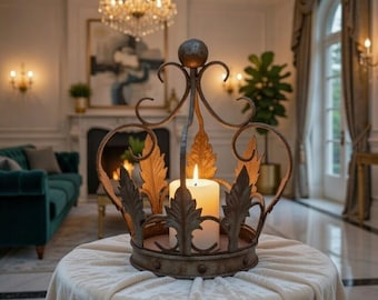 May include: A decorative, antique-style crown candle holder. The metal crown features ornate leaf and scroll designs, with a large white candle burning inside. The candle holder sits on a round table covered with a cream-colored cloth.