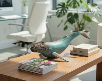 May include: A teal and brown whale figurine rests on a wooden coffee table. The whale has a textured head and tail, with outstretched fins. A stack of magazines and two books are also on the table.