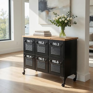 May include: Black metal cabinet with six numbered compartments, a light wood top, and decorative metal legs with wheels. The cabinet has a vintage industrial design. A vase of white tulips sits on top.
