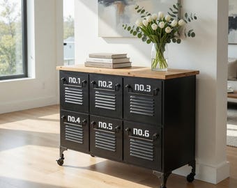 May include: Black metal cabinet with six numbered compartments, a light wood top, and decorative metal legs with wheels. The cabinet has a vintage industrial design. A vase of white tulips sits on top.