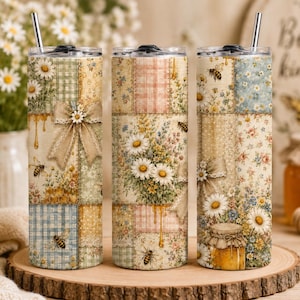 Peut inclure: Trois gobelets en acier inoxydable avec couvercles et pailles. Chaque gobelet présente un motif patchwork avec des marguerites, des abeilles et des gouttes de miel. Les gobelets ont un thème floral vintage.