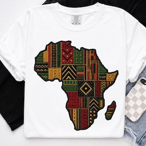May include: White t-shirt featuring a colorful, patchwork design of the African continent. The design incorporates various patterns in red, green, yellow, and black. The shirt is made of a soft material and has a crew neck.