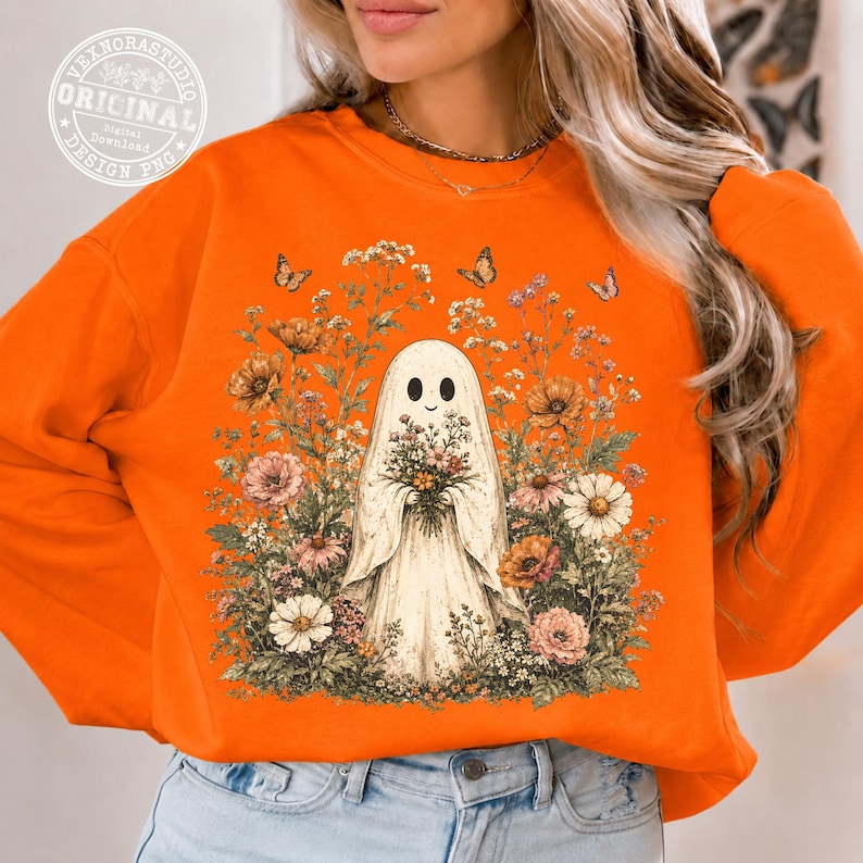 Pu&ograve; includere: Una felpa arancione con una grafica centrale raffigurante un fantasma bianco che tiene un bouquet di fiori, circondato da una fitta disposizione di fiori di campo colorati e farfalle. Il design include vari fiori nelle tonalit&agrave; rosa, arancione e bianco.