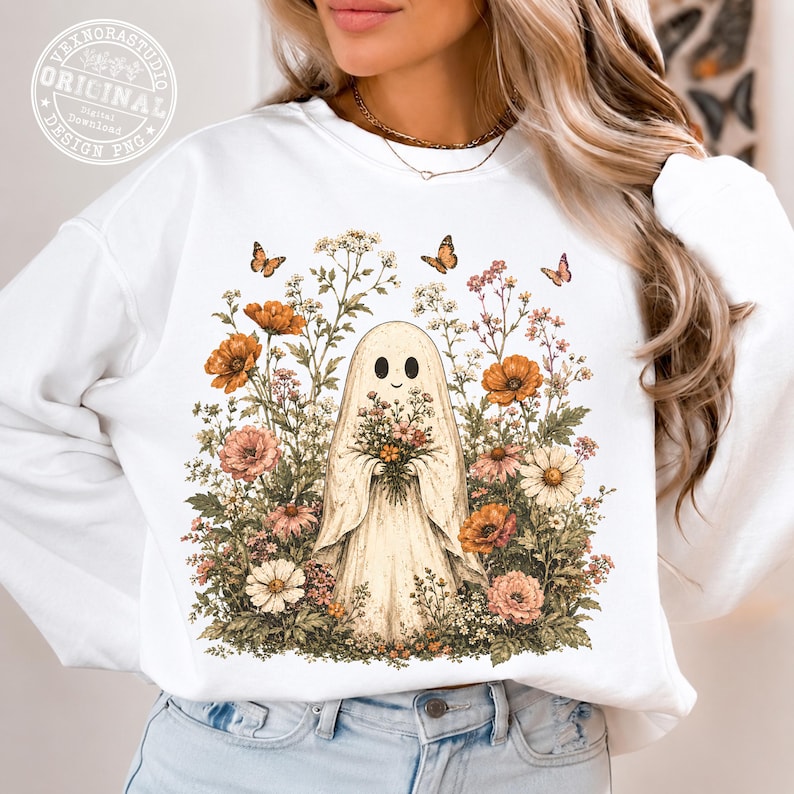 Pu&ograve; includere: Una felpa bianca a maniche lunghe con una grafica centrale raffigurante un fantasma che tiene un bouquet di fiori, circondato da una variet&agrave; di fiori di campo colorati e piccole farfalle nei toni dell'arancione, rosa e bianco, stampata sul davanti.