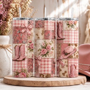 Peut inclure: Trois gobelets isothermes en acier inoxydable avec des motifs patchwork roses. Chaque gobelet présente un design différent, notamment des bottes de cowboy, un chapeau de cowboy et des motifs floraux. Les gobelets ont une paille et sont exposés sur une surface en bois.