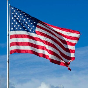 May include: A red, white, and blue American flag waving in the wind against a bright blue sky with white clouds.