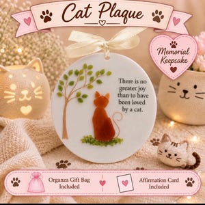 May include: A round white ceramic plaque featuring a brown cat silhouette sitting under a green tree, with the text: There is no greater joy than to have been loved by a cat. The plaque hangs from a cream ribbon and includes a gift bag and card.