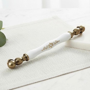 Può includere: Pomello per armadio in ceramica bianca con accenti floreali dorati ed estremità color ottone antico. La maniglia ha una forma curva, con un design floreale dorato. Ferramenta per mobili e decorazioni per la casa.