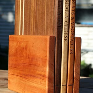 May include: A set of three rectangular wooden cutting boards stored in a matching wooden stand. The boards are labelled with engraved text reading MEAT & FISH, BREAD & CHEESE, and FRUITS & VEGETABLES, featuring varying wood tones and grain patterns.
