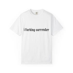以下が含まれることがあります： 黒いゴシック体で「i fucking surrender」と書かれた白いTシャツ。クルーネックと半袖です。テキストはシャツの前面の中央に配置されています。