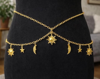 May include: Gold-colored body chain with celestial charms. The chain features sun, moon, and star pendants. The chain is draped across the waist, creating a decorative accessory.