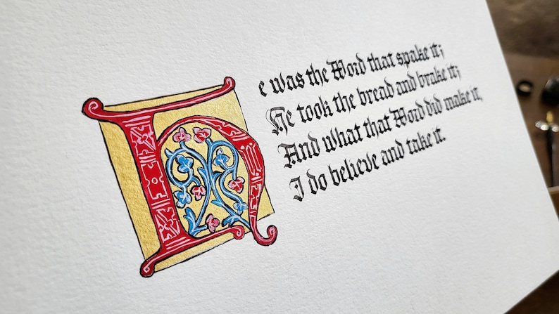 May include: A calligraphic illustration of a large red and gold letter "I" with blue and pink floral designs. The text "e was the Word that spake it; He took the bread and brake it; And what that Word did make it, I do believe and take it." is written in black ink.