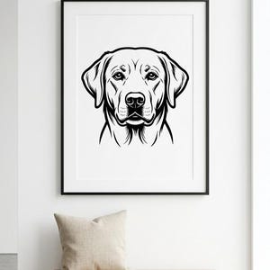 May include: A black and white framed print featuring a detailed illustration of a Labrador Retriever's face. The artwork is displayed above a wooden bench with a beige pillow, set against a white wall.