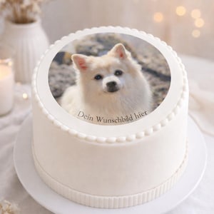 Könnte beinhalten: Ein weißer Kuchen mit einem Foto eines flauschigen weißen Hundes. Der Kuchen hat einen dekorativen Rand und der Text "Dein Wunschbild hier" ist sichtbar. Der Kuchen steht auf einem weißen Teller.