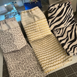 May include: Three fabric drawstring pouches featuring distinct patterns: a grey leopard print, a cream-colored bag with metallic gold wavy lines, and a black and white zebra stripe print. Each pouch has a gathered top closure with a drawstring.