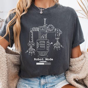 May include: Dark gray t-shirt featuring a white line drawing of a robot. The robot design includes mechanical details and the text "Robot Mode Loading" at the bottom. The shirt is a casual style.