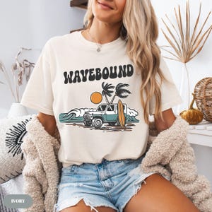 Surf club themed t-shirt graphic with vintage off road vehicle, surfboard and tropical beach waves symbolizing coastal freedom lifestyle.