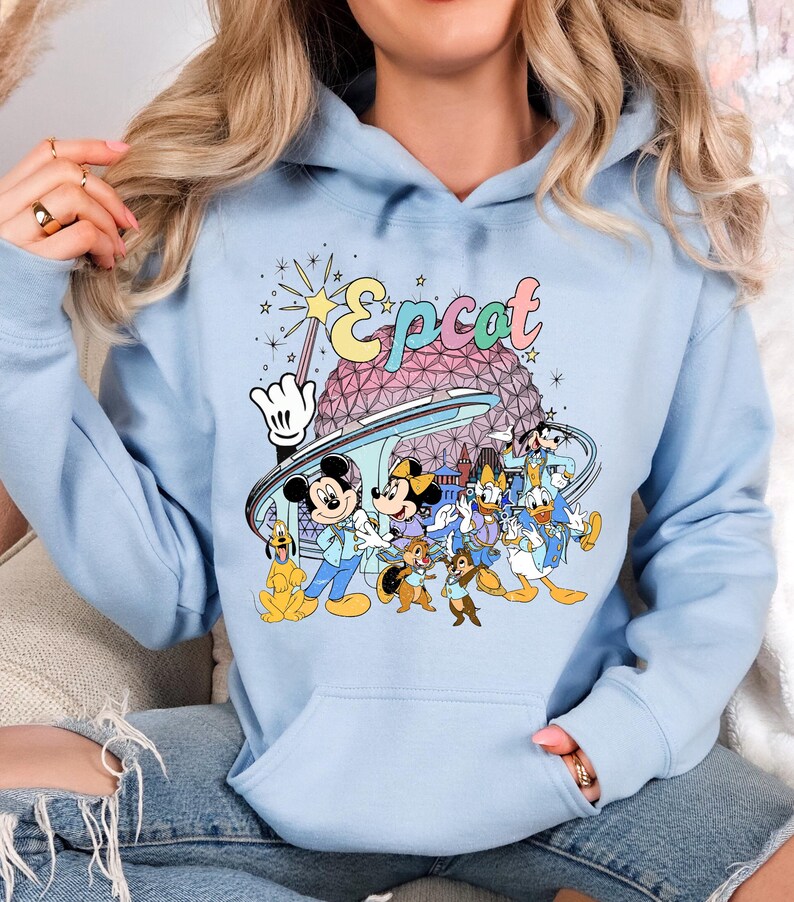 May include: Light blue hoodie featuring a colorful graphic of Disney characters, including Mickey and Minnie Mouse, Donald Duck, and Goofy, with the word "Epcot" above them. The design includes the Epcot ball and other park elements.