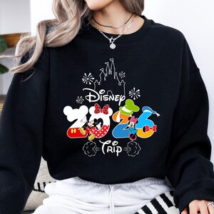 Pu&ograve; includere: Felpa nera con un design Disney colorato. Il design include il testo "Disney Trip 2026" con Topolino e Minnie, e una sagoma di castello. La felpa &egrave; uno stile girocollo.