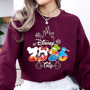 Pu&ograve; includere: Felpa bordeaux con grafica bianca del castello Disney e la scritta "Disney Trip 2026". I numeri 2026 sono disegnati con i personaggi di Topolino e Minnie. Un capo casual.