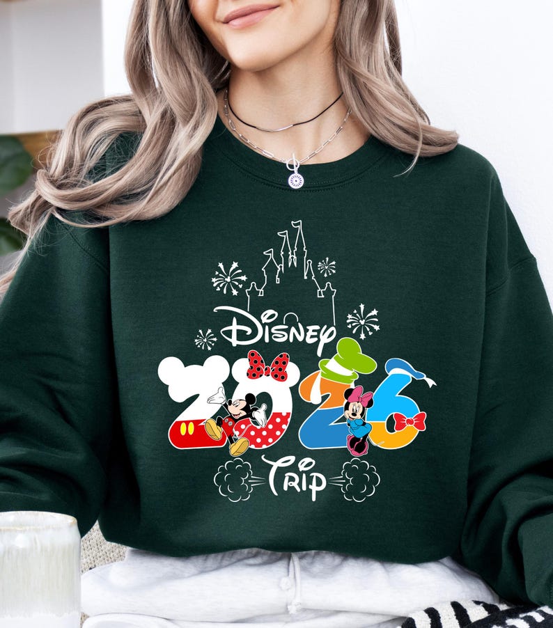 Pu&ograve; includere: Felpa verde scuro con la scritta "Disney 2023 Trip" e illustrazioni di Topolino e Minnie. Il design include una silhouette di castello e numeri colorati. Un top comodo e casual.