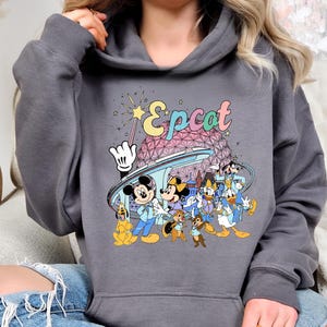 May include: Dark gray hooded sweatshirt featuring a colorful graphic of Disney characters, including Mickey and Minnie Mouse, Chip and Dale, and Donald Duck. The word "Epcot" is written in a retro font above the characters.