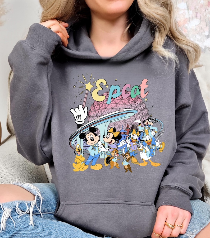 May include: Dark gray hooded sweatshirt featuring a colorful graphic of Disney characters, including Mickey and Minnie Mouse, Chip and Dale, and Donald Duck. The word "Epcot" is written in a retro font above the characters.