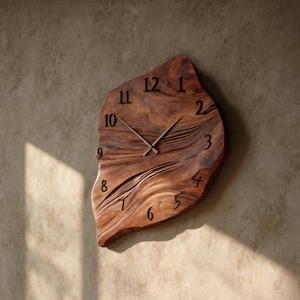 May include: A unique, wooden wall clock with a natural, organic shape. The clock face is carved from a single piece of wood, featuring a warm brown color and visible wood grain. Black numerals mark the hours, and the hands are a dark color.