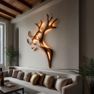 Può includere: Una scultura da parete in legno a forma di ramo d'albero con illuminazione calda. La scultura è montata su una parete di colore neutro sopra un divano chiaro con cuscini decorativi. La stanza ha un design moderno e minimalista.