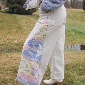 May include: Cream corduroy trousers with a patchwork quilt detail down the side. The quilt incorporates pastel shades of blue, pink, and lilac. The trousers are worn with white heeled boots.