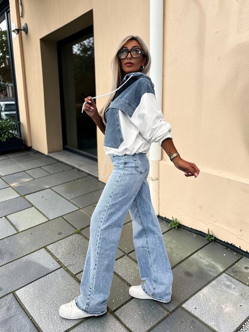 May include: A denim and white hooded jacket with matching light blue jeans and white sneakers. The jacket features a denim front and hood with white sleeves and a drawstring. The jeans are wide-legged.